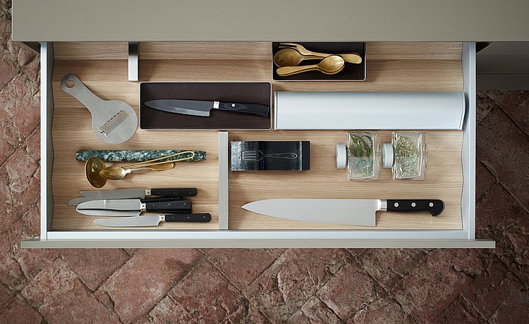 Well organized drawer with light wood prisms and equipment elements: foil roll holder, spice jars, and stainless steel dividers